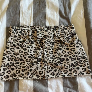 Leopardmönstrad jeanskjol Pull&Bear - Säljer en kort jeanskjol från Pull&Bear med leopardmönster i beige och svart. Kjolen har rå kant nedtill, fem fickor och dubbla silverknappar fram. Perfekt för dig som vill sticka ut med en edgy och trendig look.