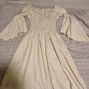 Milkmaid whimsical klänning - Säljer en ljus milkmaid klänning med breda trumpetärmar. Klänningen har smock i midjan och når strax under knäna på mig som är 170 cm. Använd en gång 