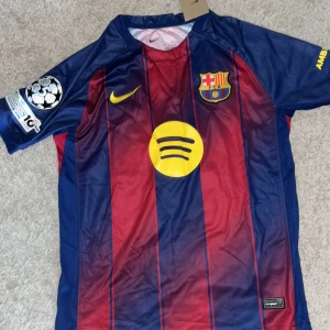 FC Barcelona Lamine Yamal matchtröja - Barça matchtröja med Lamine Yamal och nummer 10 på ryggen. Klassiska blå och röda ränder, gula detaljer och klubbmärke på bröstet. Nike-logga, Spotify som sponsor och Champions League-märke på ärmen. Tillverkad i lätt och ventilerande polyester.