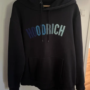 HOODRICH Hoodie  - Blå hoodie från HOODRICH med stort broderat tryck i olika blå nyanser över bröstet. Tröjan har huva med snörning, magficka och långa ärmar. Samt gömd ficka i armen.  Köptes på JD för 1,5 år sedan ungefär, säljs då jag gått ner ett par storlekar!