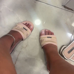 Rosa sandaler CD - Snygga sandaler, ljusrosa toner med bred rem där loggan är broderad i guld. Tjock sula med vit kant och öppen tå. Perfekta för sommardagar och ger en lyxig touch till din outfit.