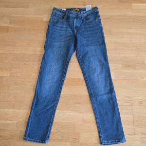 Blå jeans från Jack & Jones - Klassiska blå jeans från Jack & Jones med fem fickor, snygga kontrastsömmar och läderpatch bak i midjan. Modellen har rak passform och normal midja. Perfekta till vardags med en t-shirt eller hoodie. Strl 164, 14 Y.