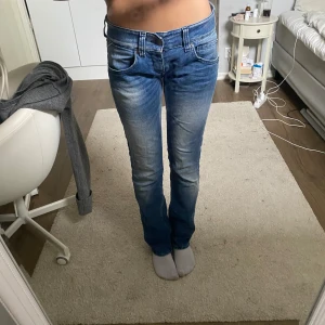 Blå Replay jeans lågmidjade - Säljer ett par snygga blå jeans från Replay med bootcut-modell. Jeansen har klassisk femficksdesign, låg midja och lätt slitna detaljer framtill och baktill. Materialet är mjukt jeans i bomull, perfekta för en avslappnad look.