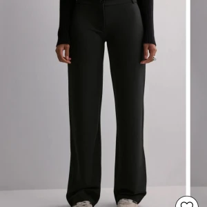 Svarta vida kostymbyxor - Snygga svarta kostymbyxor med låg midja och raka, vida ben från Nelly. Byxorna har klassisk passform och stängs med knapp och dragkedja. Dem är aldrig använda, endast testade. Säljer då dem va för små till mig. Etiketten är kvar.