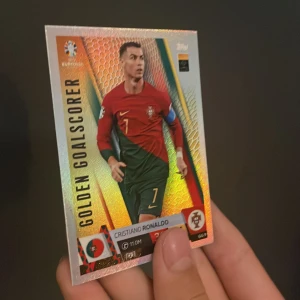 Golden Goalscorer - Cristiano Ronaldo (UEFA Euro 2024 Match Attax) - Samlarbild från UEFA Euro 2024 Match Attax med Cristiano Ronaldo i Portugals landslagströja. Perfekt för unga fotbollsfans och samlare som vill ha en glänsande och cool kort på en av världens största stjärnor. (Limited Editon)
