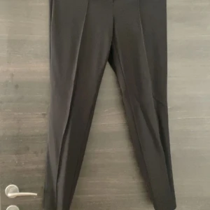 Svarta kostymbyxor med smal passform - Snygga svarta kostymbyxor med smal och rak passform. Byxorna har pressveck framtill och är perfekta för en clean och stilren look. Materialet känns mjukt och följsamt, vilket gör dem bekväma att bära hela dagen.