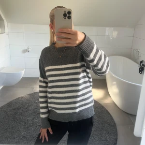 Randig grå och vit stickad tröja Shein - Mysig stickad tröja från Shein i storlek XS. Tröjan är grå med vita horisontella ränder, har rund hals och långa ärmar. Perfekt för lager-på-lager och chill dagar. Snygg till både jeans och kjol.