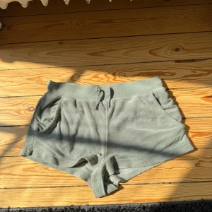 Gröna frottéshorts Juicy Couture XS - Mysiga ljusgröna shorts från Juicy Couture i frotté med bred midja och snörning framtill. Modellen har två fickor och är tillverkad i mjuk bomull och polyester. Perfekta för chill dagar eller när du vill ha en comfy vibe.