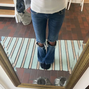 Blå bootcut jeans med slitna knän - Säljer ett par blå jeans med bootcut passform och slitna hål vid knäna från Lager 157. Jeansen har klassisk femficksdesign och är tillverkade i jeansmaterial med en snygg mörkblå ton. Använda max 5 gånger