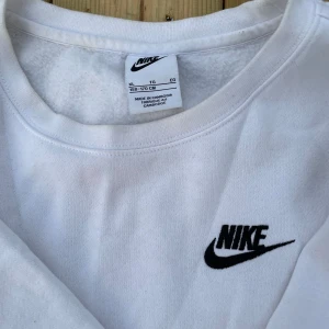 Vit långärmad Nike sweatshirt XL - Klassisk vit sweatshirt från Nike i storlek XL med svart broderad logga på bröstet. Tröjan har rund halsringning och långa ärmar. Tillverkad i mjuk bomullsmix som är skön att ha på sig. Perfekt för en clean och sportig look. pris diskuteras 158 170