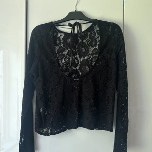 Svart spetsblus från BikBok XS - Svart blus från BikBok i storlek XS, helt i blommig spets med lång ärm och snygg knytning i nacken. Aldrig använd
