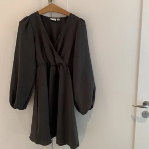 Svart omlottklänning med puffärm - Snygg svart/grå kortklänning från VILA med omlott-design och v-ringning. Klänningen har långa puffärmar och ett lätt rynkat midjeparti som ger en skön passform. Materialet är mjukt och har en diskret struktur som gör den extra cool.Storlek 34 men rymlig gör storlek och modellen känns inte liten.Väldigt skön och samtidigt elegant.