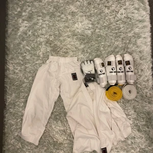 Karatedräkt och taekwondodräkt  med skydd och bälten - Hej! Jag säljer en taekwondo och karatedräkt i vitt från budo-nord komplett med jacka och byxor i bomull. Inkluderar fyra vita benskydd från budo-nord, ett par vita handskar från kaiwende samt ett gult och vitt bälte perfekt för dig som tränar karate eller taekwondo och vill ha allt i paket. 
