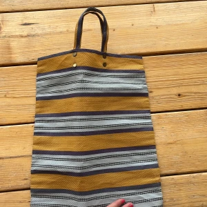 Randig shoppingväska i bomull - Säljer en randig shoppingväska i bomull med gula, gråa och svarta ränder. Väskan har två handtag och är perfekt att bära till skolan eller stan. Enkel och stilren design med mjukt tyg och rymligt fack.