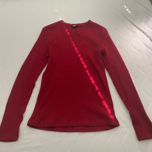 Röd ribbad tröja från Dolce & Gabbana - Snygg röd långärmad tröja från Dolce & Gabbana i ribbad bomull. Tröjan har en klassisk rund hals och ett stilrent D&G-märke på ryggen. Perfekt för dig som vill ha en enkel men lyxig look med lite edge. Står XL men passar även L