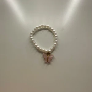 Pärlarmband med fjärilshänge - Superfint armband med vita pärlor och en söt fjäril som hänge. Finns i två varianter: en med ljusrosa fjäril och en med guldfärgad fjäril. Perfekt accessoar för dig som gillar gulliga detaljer.🫶🏻