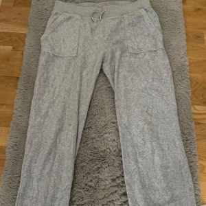 Grå mjukisbyxor Juicy Couture L - Supermjuka grå mjukisbyxor från Juicy Couture med snörning i midjan och stora fickor fram. Baksidan har två fickor med knappdetalj. Säljer då dom ej används.