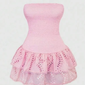 Rosa axelbandslös kort klänning - Supersöt rosa klänning med smockad överdel och axelbandslös design. Kjolen är kort med två lager volanger och broderade detaljer som ger en lekfull vibe. Perfekt för dig som vill sticka ut med en feminin och trendig look.