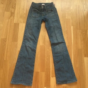Blå bootcut jeans från Nelly - Snygga blå jeans från Nelly med bootcut passform och låg midja.  Jeansen har markerade sömmar längs benen och coola fickor framtill. Väldigt bra i skick. Säljer för de tyvärr har blivit för små för mig