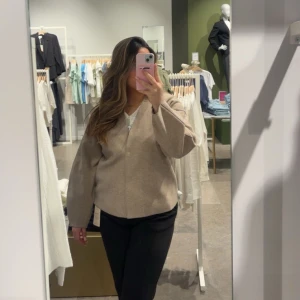 Beige jacka med v-ringning - Snygg beige kofta med v-ringad hals och långärmade, lite vidare ärmar. Enkel och stilren design som passar till många olika outfits. Materialet känns mjukt och har en lätt struktur, perfekt för lager-på-lager under kyliga dagar. Helt oanvänd prislapp finns kvar. 