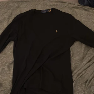Svart långärmad tröja Polo Ralph Lauren - Svart långärmad tröja från Polo Ralph Lauren i slim fit-modell. Klassisk design med rund hals och den ikoniska broderade loggan på bröstet. Perfekt för dig som gillar stilrena och enkla plagg med premiumkänsla. Materialet är mjuk bomull som känns skönt mot huden.