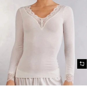 Vit långärmad topp med spetsdetaljer - Supersöt vit långärmad topp med v-ringning och fina spetsdetaljer vid halsringning och ärmslut. Sitter tight och har en feminin, elegant vibe. Perfekt att styla med både jeans och kjol för en chic look. Är som helst ny, orgnial pris 490kr. 