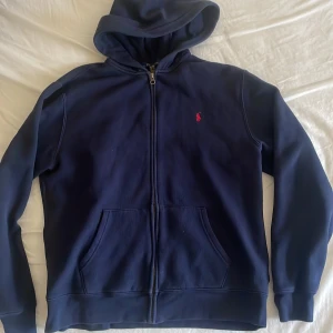 Marinblå hoodie från Polo Ralph Lauren - Säljer en marinblå hoodie från Polo Ralph Lauren i storlek S. Tröjan har dragkedja, huva och fickor framtill. Klassisk röd Polo-logga på bröstet. Nyskick🌟