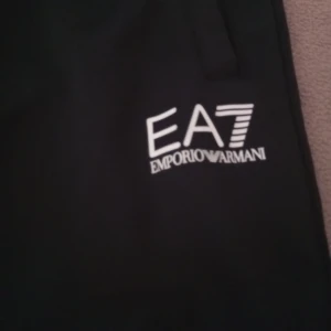 Svarta mjukisbyxor EA7 Emporio Armani - Svarta mjukisbyxor från EA7 Emporio Armani med vit logga på benet. Byxorna har en sportig look, resår i midjan och är tillverkade i ett mjukt material som passar perfekt för chill eller träning.
