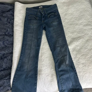 Blå bootcut jeans från Nelly - Snygga blå jeans från Nelly med bootcut-modell och låg midja. Jeansen har markerade sömmar längs benen, dubbla framfickor med dragkedjedetaljer och klassiska bakfickor. Perfekta för dig som gillar en retro vibe och vill ha något som sticker ut. Jag är inte säker men tror den är i storlek 36, den är iaf för 152 cm.