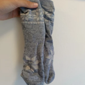 Gråa ullstrumpor med mönster - Mysiga gråa ullstrumpor med vitt nordiskt mönster upptill och vid foten. Perfekta för kalla dagar och har en klassisk vinterstil. Tjocka och varma, passar bra i boots eller hemma.
