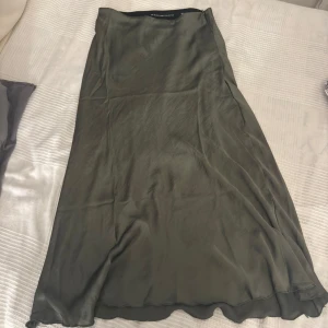 Olivgrön kjol från lager 157 - Säljer olivgrön kjol från lager 157 i storlek M. Kjolen har en mjuk, glansig yta och är lätt utsvängd med dragkedja i sidan. Kjolen är köpt för 200 kr och aldrig använd. 