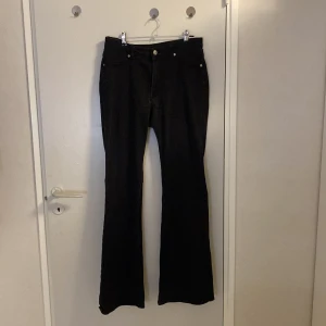 Svarta bootcut jeans från H&M Divided - Svarta jeans från H&M Divided i bootcut-modell med klassisk femficksdesign. Byxorna har normal passform upptill och utsvängda ben, vilket ger en snygg siluett. Perfekta för dig som gillar en retrovibe och vill ha ett par stilrena svarta jeans.