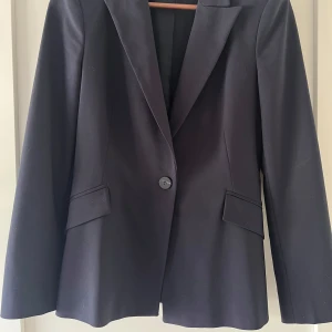 Mörkblå  kavaj från Zara Basic, M - Klassisk mörkblå kavaj från Zara Basic i storlek M. Enkelknäppt modell med snygg krage och två fickor med lock framtill. Stilren och tidlös design som passar till många olika looks. Tillverkad i ett mjukt och följsamt material.