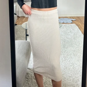 Beige ribbad kjol - Snygg beige ribbad kjol i midi-längd. Kjolen har en tight passform som framhäver figuren och är perfekt för en stilren look. Den är tillverkad i ett mjukt och stretchigt material som ger komfort hela dagen.