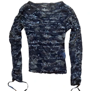 Camouflage långärmad topp med textmönster - Säljer en unik långärmad topp med ett coolt textmönster i vitt över en mörk camouflagebas. Snörning vid armarna så man kan dra och justera längden på ärmarna. Strl M på lapp men mer en XS eller S i storlek. 