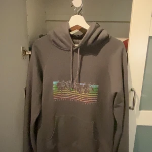 Saint Laurent Hoodie - Säljer en snygg grå hoodie från Saint Laurent med ett färgglatt tryck av palmer och texten 'Malibu Saint Laurent' på framsidan. Hoodien har en klassisk passform med långa ärmar. Har annat som hägrar kan prisförhandla