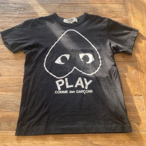 Svart t-shirt från Comme des Garçons - Säljer en svart t-shirt från Comme des Garçons med det ikoniska hjärtmotivet och texten 'PLAY' på framsidan. T-shirten är i storlek M men passar mer som S.