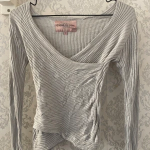 Grå ribbad omlottopp från C'est la vie - Grå ribbad omlott tröja! Den är i bra skick förutom ett hål uppe vid nacken,Storlek 134/140 💕🙌