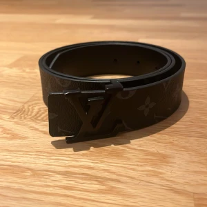 Svart bälte  - Snyggt svart bälte med klassiskt monogrammönster. Bältet har en stilren spänne i svart metall. Tillverkat i Frankrike, perfekt för att ge din outfit en lyxig touch.