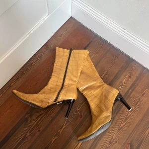 Gula stövletter med krokodilmönster - Snygga gula stövletter med krokodilmönster och spetsig tå. De har en elegant klack och dragkedja på sidan för enkel på- och avtagning. Perfekta för att ge en färgklick till din outfit.