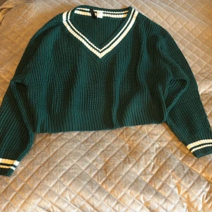Grön ribbad tröja från H&M - Grön ribbad tröja från H&M med vita ränder vid v-ringningen och ärmsluten. Tröjan har en croppad passform och långa ärmar. Perfekt för en stilren look! 💚
