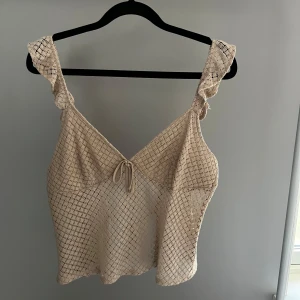 Beige spetslinne från H&M Divided - Säljer ett superfint beige spetslinne från H&M Divided. Linnet har en v-ringad design med knytning fram och volangdetaljer vid axlarna. Perfekt på sommaren.