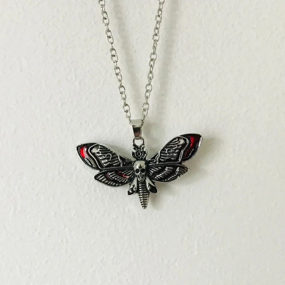 Unikt halsband med ett detaljerat fjärilshänge i silverfärg med röda inslag. Kedjan är av metall och har en klassisk länkdesign. Perfekt för att ge en edgy touch till din stil.. Asusteet.