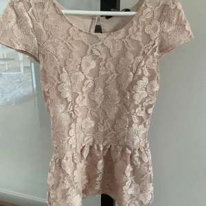 spetsblus  - Säljer en elegant beige/rosa spets blus från Dorothy Perkins. Blusen har korta ärmar och ett vackert blommigt mönster. Perfekt för speciella tillfällen med sin feminina design och fina detaljer. Fint skick, endast små bläck fläckar som knabbt syns. Storlek: XS då jag sytt in den. 