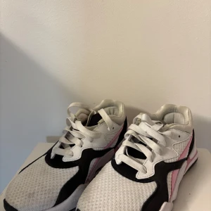 Vita och svarta sneakers med rosa detaljer - Säljer ett par snygga sneakers i vitt och svart med coola rosa detaljer. De har en sportig look med snörning och är perfekta för både vardag och träning. Skorna är i bra skick och har en bekväm passform. Perfekta för dig som vill ha stil och komfort i ett!