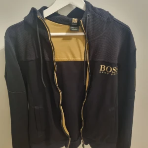 Svart hoodie från Hugo Boss - Svart hoodie från Hugo Boss med dragkedja och huva. 