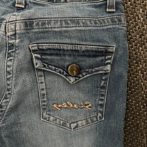 Blå jeans från Sisley - Snygga blå jeans från Sisley med en klassisk femficksdesign och knappdetaljer. De har en bootcut-stil som ger en avslappnad look. Perfekta för en casual outfit.