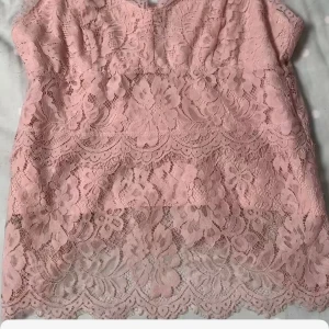 Rosa spetslinne - Säljer ett romantiskt rosa spetslinne med vacker blommig design. Toppen är ärmlös och perfekt för sommarens varma dagar. Den har en elegant och feminin stil som passar till många olika tillfällen.