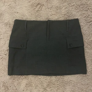 Grå kortkjol med fickdetaljer - Snygg grå kortkjol med praktiska fickor framtill och knappdetaljer