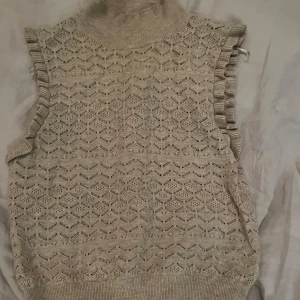 Beige stickad väst med volangdetaljer - Säljer en beige stickad topp med ett fint mönster och volangdetaljer vid ärmhålen. Perfekt  nu till våren  och sommaren. Inga defekter och köp gärna med köp nu. 😊